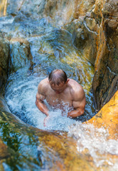 Bathing of the young man under waterfall.