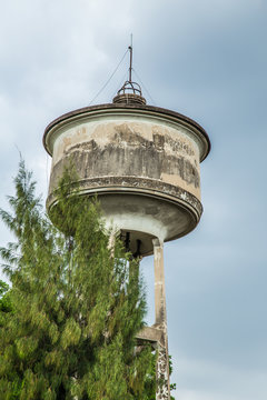old concrete water tower with lightning rod with tree and cloudy sky.