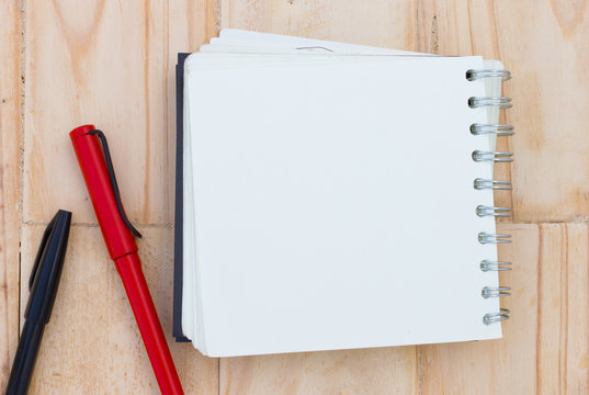 closeup blank notebook on a brown wooden table, with red and black pen