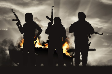 Silhouette of terrorist holding rifle against burning tank - obrazy, fototapety, plakaty