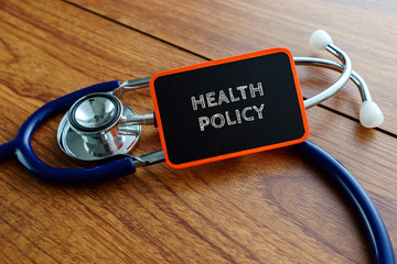 Medical concept.Word HEALTH POLICY with stethoscope on wooden table.