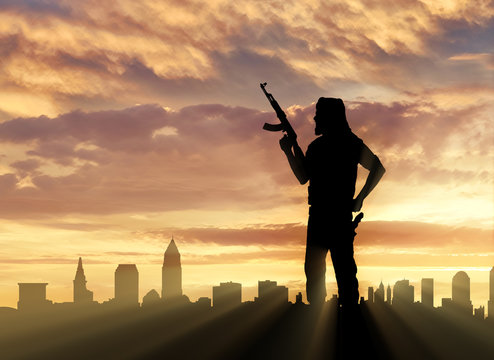 Silhouette of man with rifle standing against city during sunset