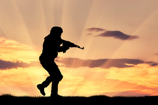 Silhouette of man with rifle against cloudy sky during sunset