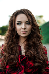 Beautiful young hipster girl posing and smiling near urban wall background in red plaid shirt, shorts, outdoors summer portrait.