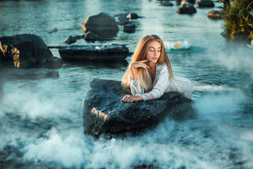 Fairy lies on a stone in water..Lake shrouded in mist. Fantastic picture. Fashionable toning