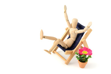 wooden mannequin sunbathing in garden with chair and beach cha