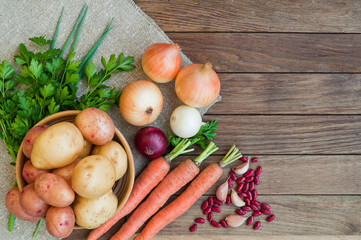 Potatoes, carrots, onions on the sacking and wooden table