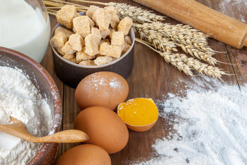Selection of all necessary products for the preparation of dough - milk, butter, eggs, sugar, flour. On wooden table