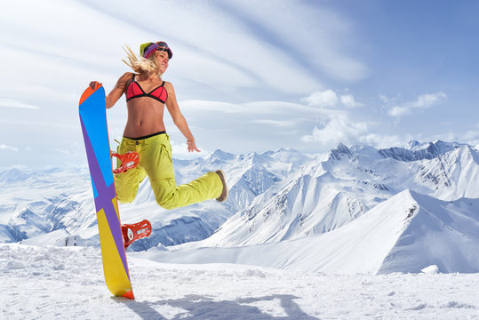 Happy young woman with snowboard jumping in winter sportswear