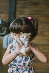 cheerful little girl holding a frightened cat in hands