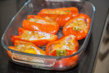 Cooked stuffed red peppers with eggs, ham and croutons in a glass oven proof serving dish.