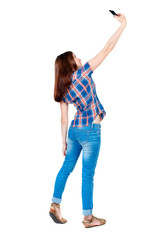 back view of standing young beautiful  woman  using a mobile phone. girl  watching. Rear view people collection.  backside view of person.  Isolated over white background. Girl in a plaid shirt is