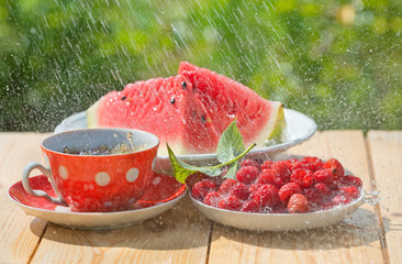Watermelon slices, ripe raspberries and cup of tea  in pouring r