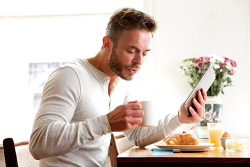 Older man drinking coffee with breakfast and holding tablet