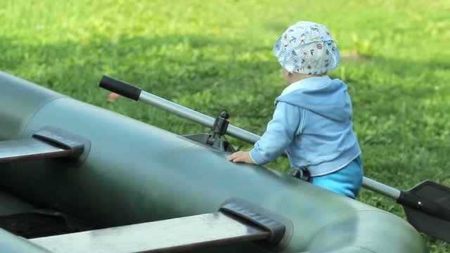 Beautiful baby boy playing with an inflatable boat and a paddle. The boat is on the grass in the garden. Growing future fisherman