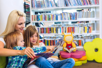 Mother with little girl and boy read book together in library