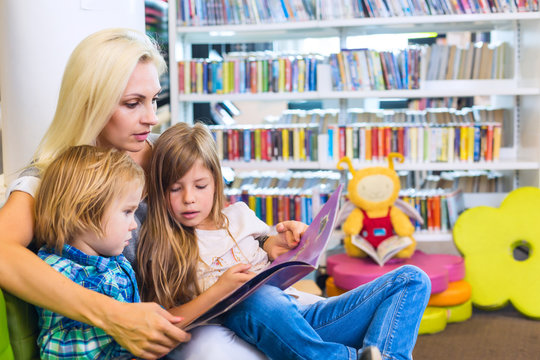 Mother with little girl and boy read book together in library