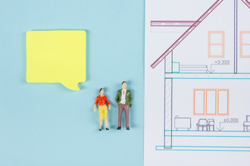 Real Estate concept. Construction building. Blank speech bubbles, people toy figures, paper model house, blueprints with key on blue architect desk table background. Top view. Copy space for ad text.