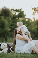 Happy young mother having fun, bowl, rising up, piggyback ride her child in park on summer sunset	