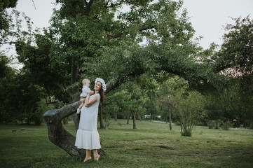 Happy young mother having fun, bowl, rising up, piggyback ride her child in park on summer sunset	