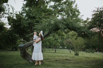 Happy young mother having fun, bowl, rising up, piggyback ride her child in park on summer sunset	