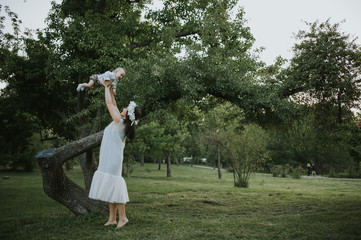 Happy young mother having fun, bowl, rising up, piggyback ride her child in park on summer sunset	