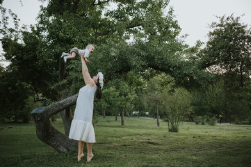 Happy young mother having fun, bowl, rising up, piggyback ride her child in park on summer sunset	