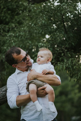 Fototapeta premium Happy young father having fun, bowl, rising up, piggyback ride his child in park on summer sunset 