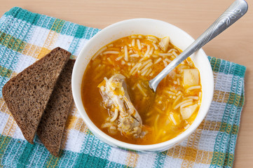 A plate of chicken soup with noodles and two pieces of bread on the table