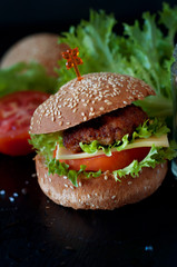 Hamburger with salad, tomato, meat on black  backdrop