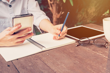 asian woman hand holding phone and pencil writing notebook in co