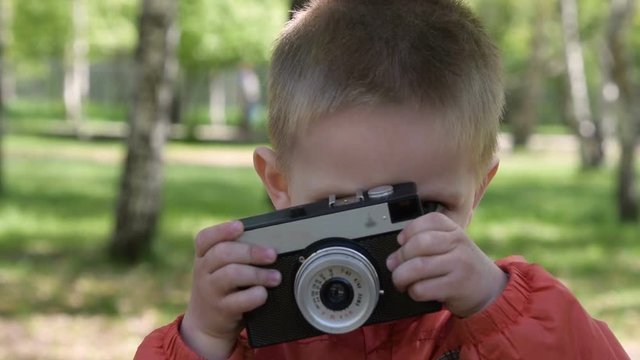 Close-up shot of cute little boy with retro camera in the park