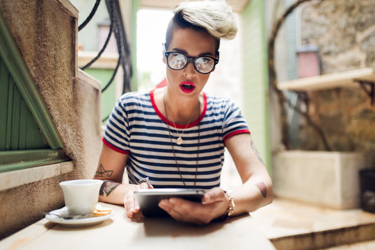 Shot of a trendy young woman with open mouth using a digital tablet in a cafe.