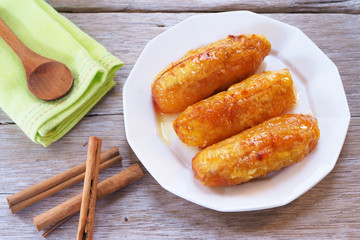 Top view of baked bananas with honey on a white plate on a wooden table.
