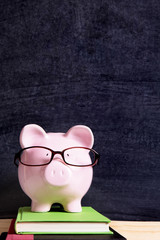 Piggybank or piggybank wearing glasses in front of a school or college blackboard education saving...