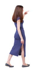 back view of pointing walking  woman. going girl pointing.  backside view of person.  Rear view people collection. Isolated over white background. The brunette in a blue striped dress goes on the side