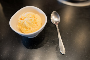 scoop of vanilla ice cream in bowl with steel spoon on dark background