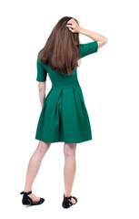 back view of standing young beautiful  woman.  girl  watching. Rear view people collection.  backside view of person. The slender brunette in a green short dress thoughtfully scratching his head.  
