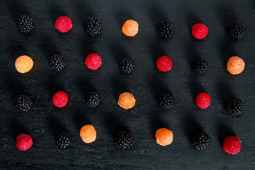 Mixed of red, black, yellow raspberries on black table. Close up.