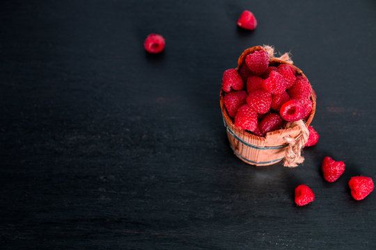 Red raspberries in a basket on black wooden background. Frame. Copy space. Top view.