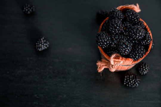 Black raspberries in a wooden basket on black wooden background. Frame. Copy space. Top view.