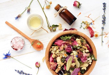 Herbal blend of various dried medicinal flowers, essential oil, bottle, sea salt. Natural skincare. Top view, focus on wooden bowl with colorful plants.