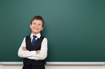 school student boy posing at the clean blackboard, grimacing and emotions, dressed in a black suit, education concept, studio photo