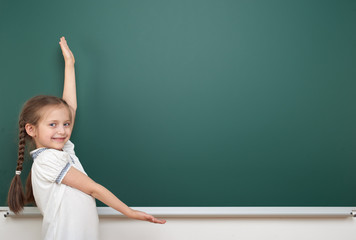 school student girl posing at the clean blackboard, grimacing and emotions, dressed in a black suit, education concept, studio photo