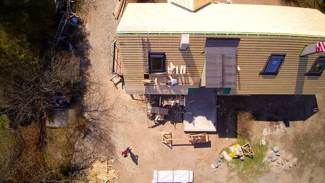 Aerial view of the wooden roof of the cabin house with a roofer installing shingles on the roof