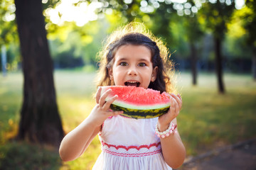 Funny kid eating watermelon outdoors in summer park, focus on eyes. Child, baby, healthy food....
