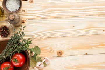 clay plate with tomatoes, herbs, thyme, rosemary, sea salt, olive oil in clay jug, garlic,  pepper, bay leaf on wooden background, top view