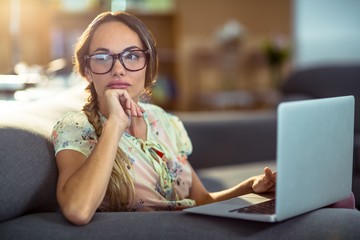 Thoughtful woman sitting on sofa and using laptop