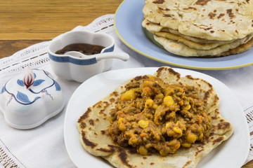 Chick pea and lentil curry with roti and chutney on white lace