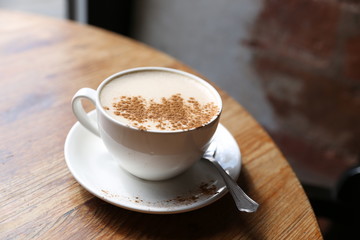 Cup of tasty latte is standing on the wooden textured table with the brick wall background.  Latte is in the white big cup.